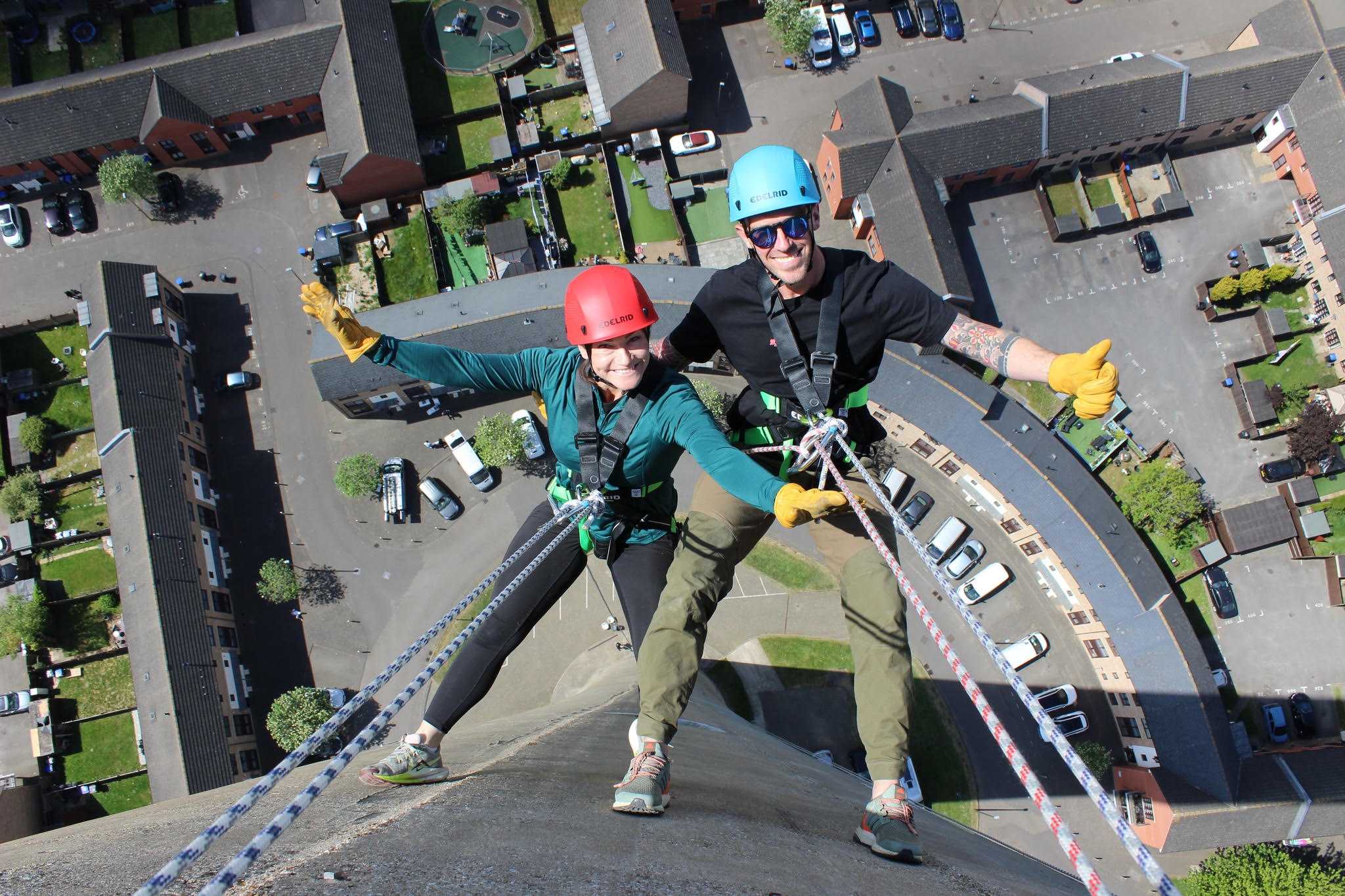 Two smiling participants abseiling together, with their hands, helmets and feet visible above Northampton