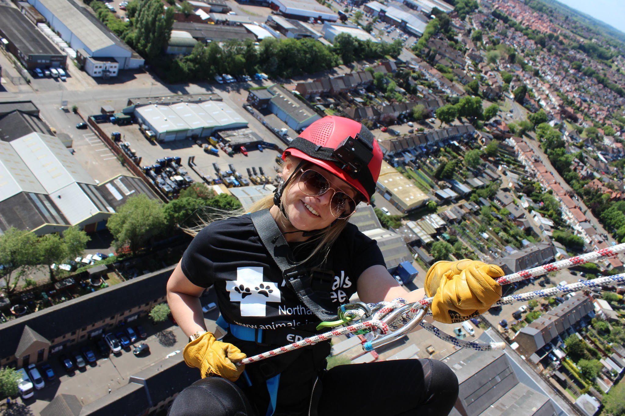 A smiling Animals in Need supporter in a red helmet abseiling high above Northampton