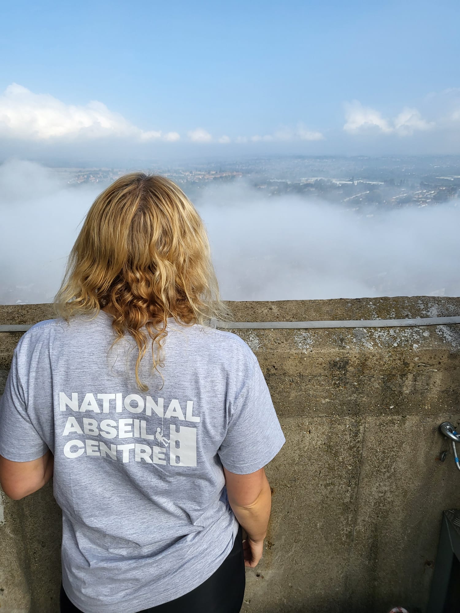 Kelly in a National Abseil Centre T-shirt looking over Northampton above the clouds from the National Lift Tower